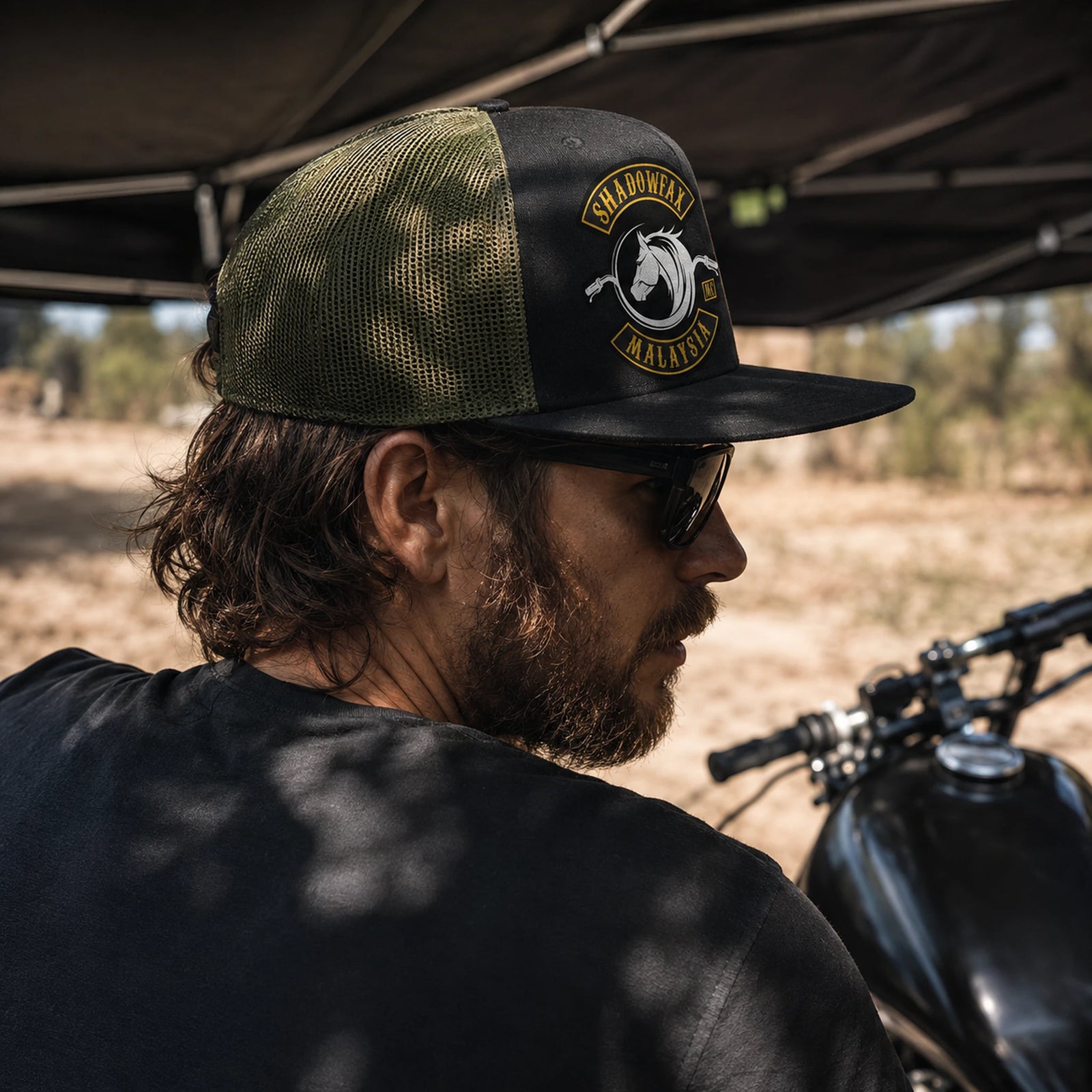 A motorcycle club rider wears a flat-brim cap with a structured front and breathable olive mesh back.