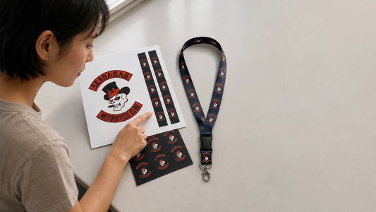 A designer checking a motorcycle club lanyard sample against its matching front-and-back artwork proof.
