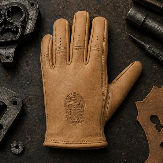A tan motorcycle club glove shows a compact bandana-skull emblem pressed into leather below the knuckles.