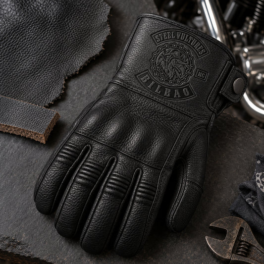 Black full-finger cowhide leather glove with defined natural grain with restrained motorcycle club branding in dark slate material review surface with a cowhide swatch and edge sample.