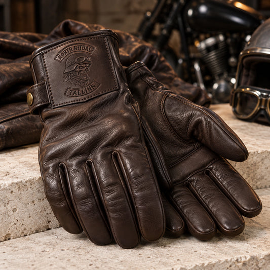 Dark chocolate full-finger sheepskin leather glove with soft smooth drape with restrained motorcycle club branding in light limestone sample plinth with soft leather folds.