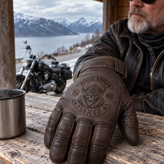 Dark brown full-finger goatskin leather glove with restrained motorcycle club branding in wooden roadside shelter overlooking a cold fjord road.