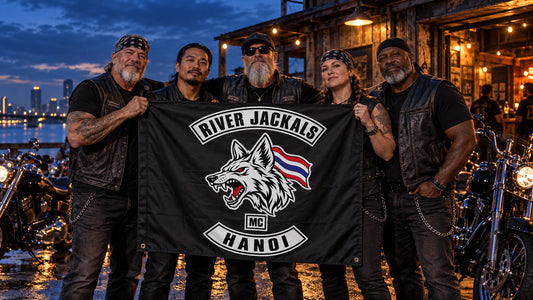 Mature V-twin riders hold a finished River Jackals square club flag together at blue hour.