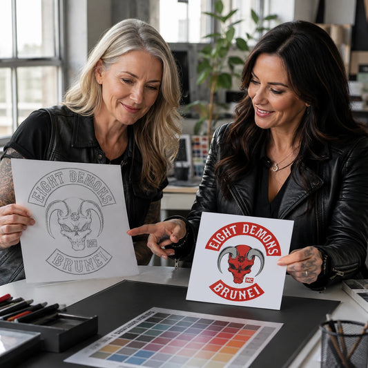 A designer and mature motorcycle club rider compare a sketch with a polished square flag concept.