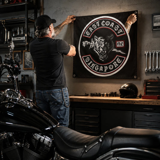 A mature rider mounts a custom motorcycle club square flag above a garage workbench.