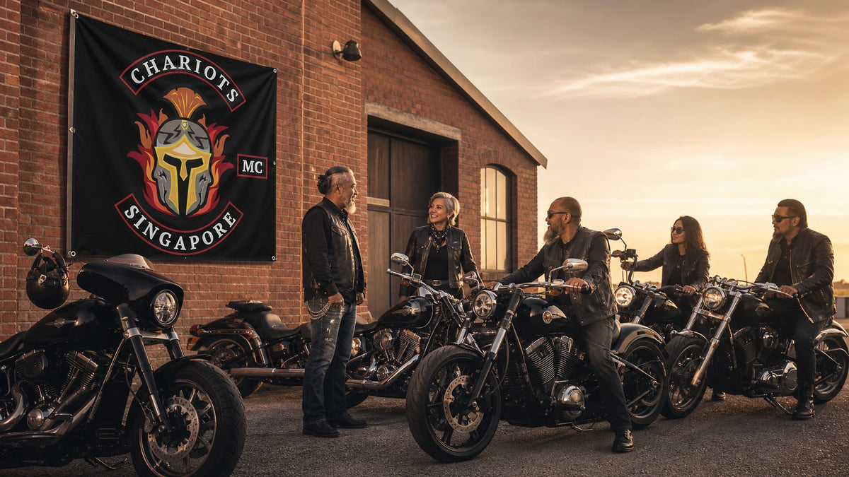 Mature motorcycle club riders beside American V-twin motorcycles and a custom square club flag on a brick clubhouse wall.