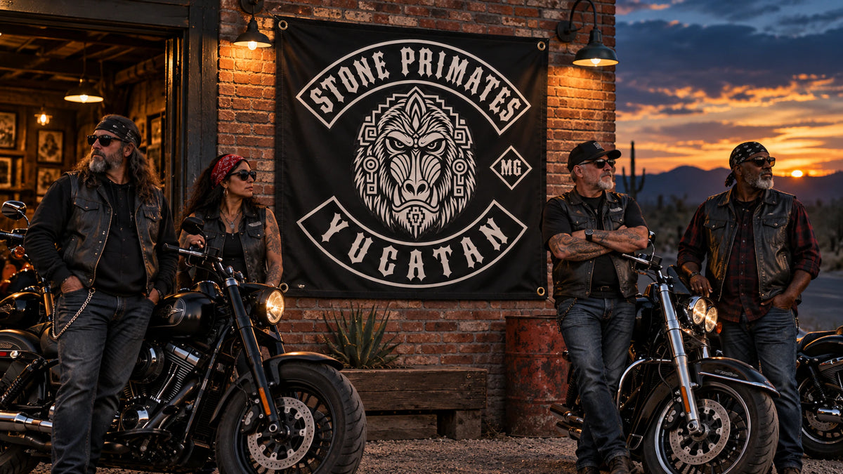 Mature V-twin riders beside a custom Stone Primates square club flag at a brick roadside clubhouse.