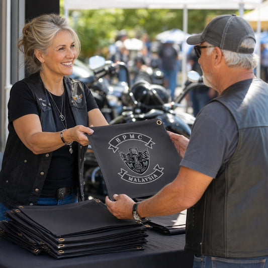 A motorcycle club volunteer hands a custom square flag to a member at a rally merchandise booth.