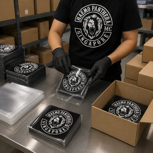 Packing operator organizing finished motorcycle club sticker sheets into cartons for worldwide shipping.