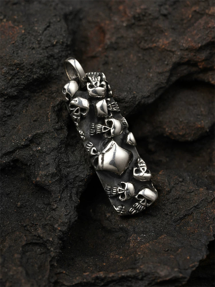 Multi-skull sterling silver biker pendant shown from the front on a dark rock background