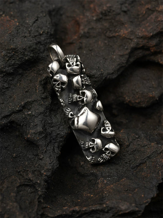 Multi-skull sterling silver biker pendant shown from the front on a dark rock background
