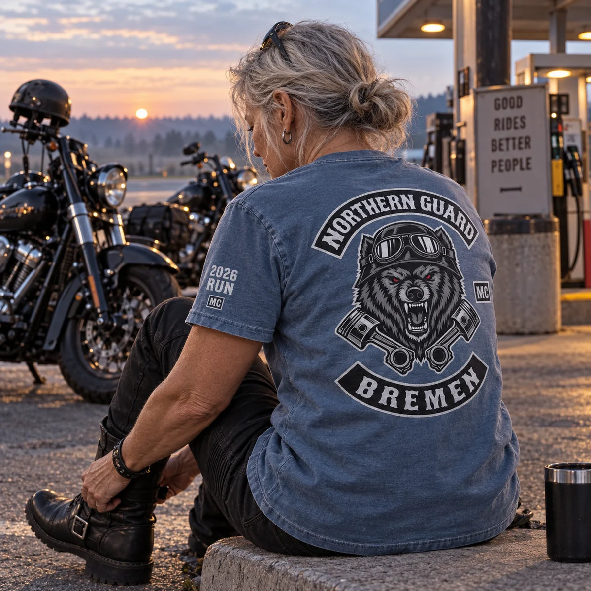 Northern Guard Bremen rider wearing a faded-blue garment-dyed club T-shirt with a compact 2026 Run sleeve print at a dawn fuel stop.