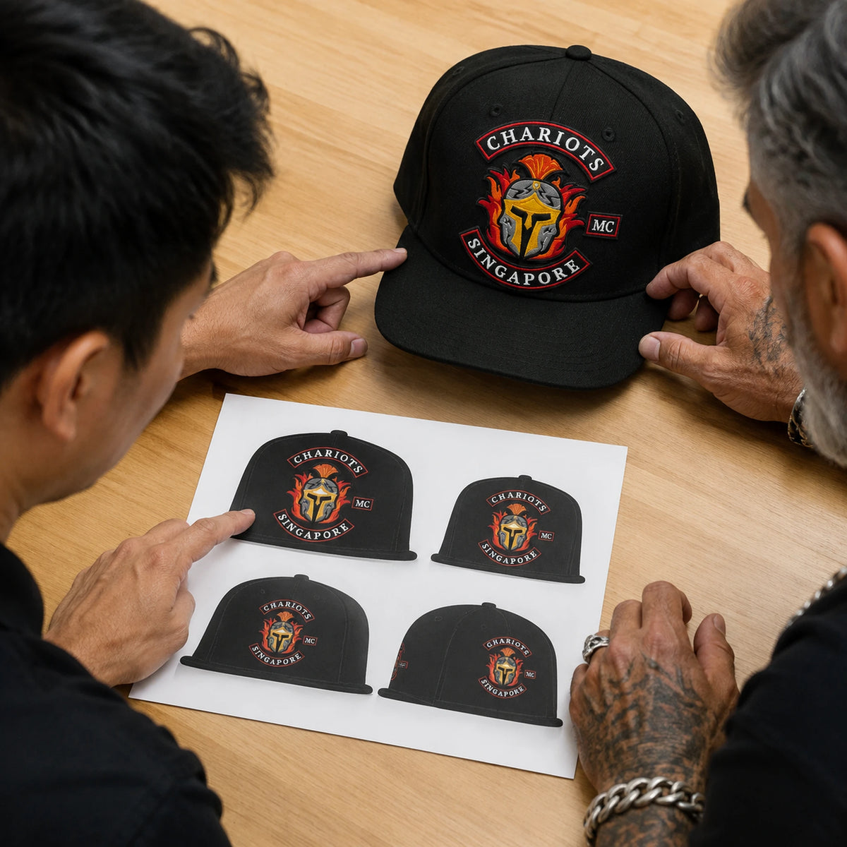 A motorcycle club rider reviews an approved emblem placement proof beside a black flat-brim cap.