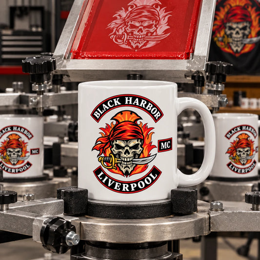 Complete ceramic mug secured in a rotary screen-printing fixture, freshly printed one-color club emblem clearly visible, machinery shown without operators.