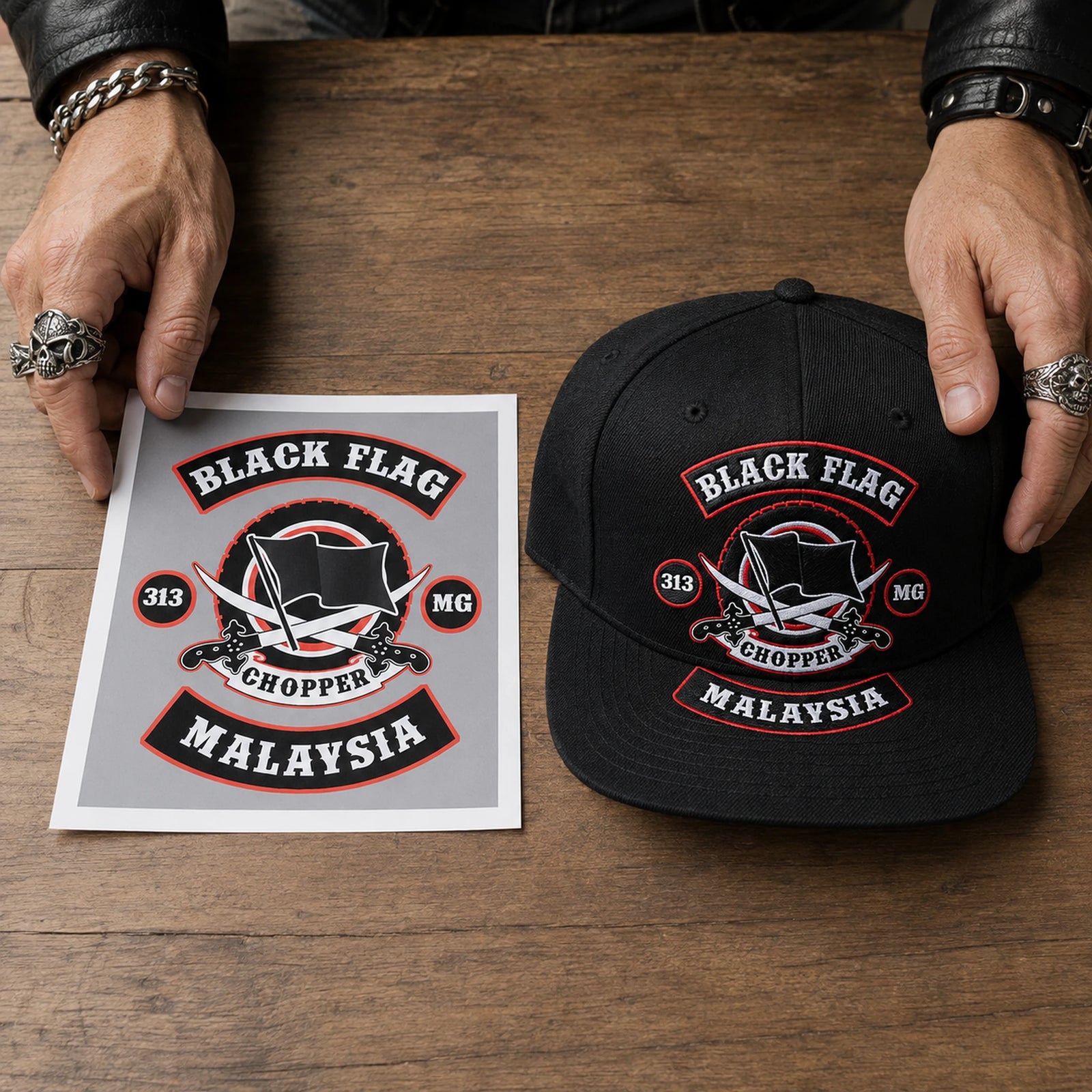 A motorcycle club rider prepares an approved emblem reference beside a black flat-brim cap for design intake.