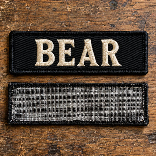 Front and back views of a sew-on motorcycle club name bar showing a clean unfinished backing edge and stitch-ready border on a leather workbench, showing custom motorcycle club name bar patch options.