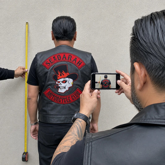 Straight rear photograph of a motorcycle vest with measuring tape visible for patch sizing.