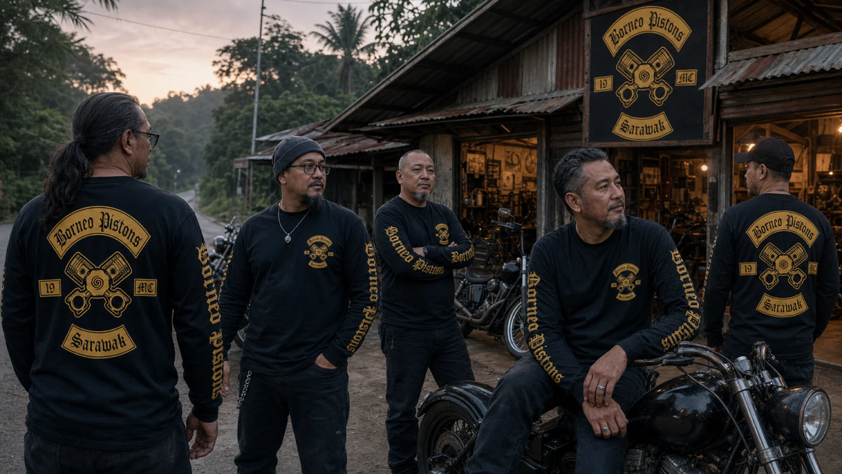 Mature American V-twin riders wearing coordinated custom motorcycle club long-sleeve shirts outside a dark clubhouse.